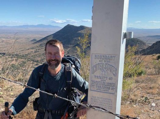 Author Tom Zoellner with backpack standing next to U.S.-Mexico border monument