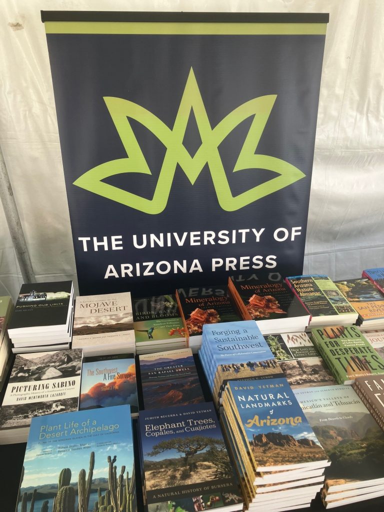 University of Arizona Press logo on a banner behind a table of books in a tent at the Tucson Festival of Books