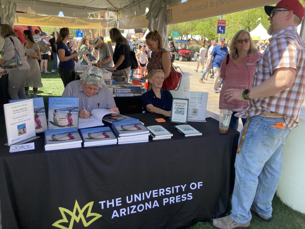 Two University of Arizona Press authors seated at a table. The one on the left signs a book.