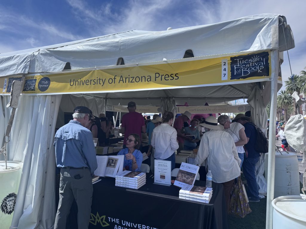 People gather around a table where a University of Arizona Press author is seated to sign books.
