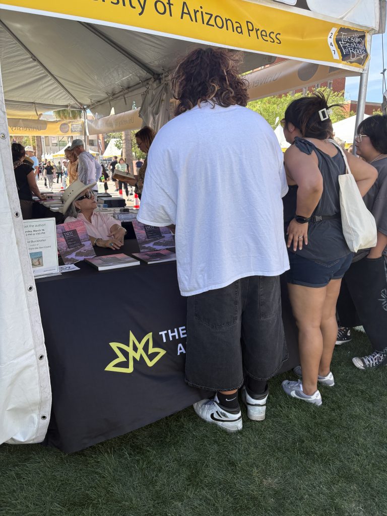 People gather around a table where a University of Arizona Press author is seated to sign books.