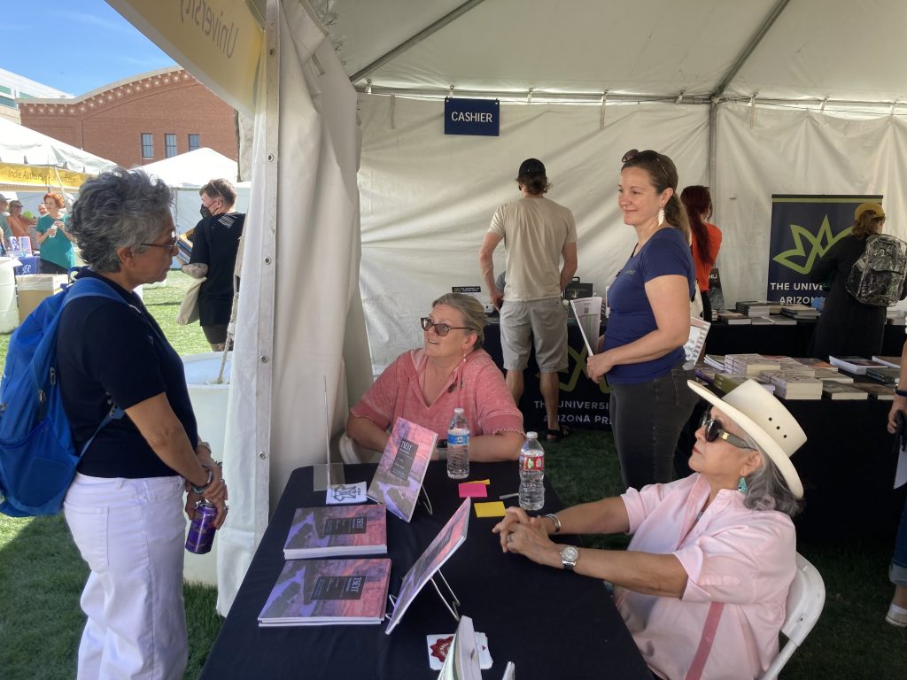 People gather around a table where a University of Arizona Press author is seated to sign books.