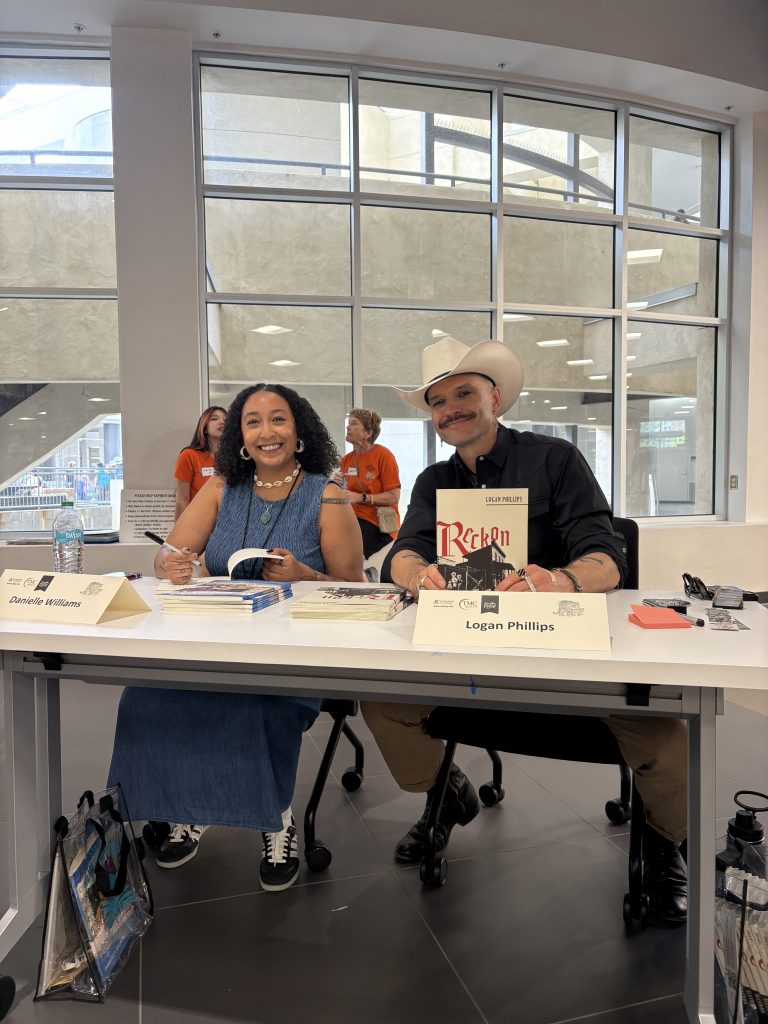 A woman signs a book at a table and a man in a cowboy hat holds up his book, the title "Reckon" in red letters